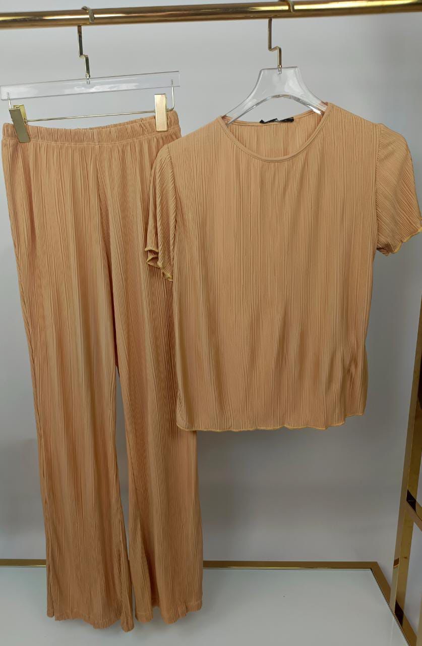 Beige top and pants set hanging on a rack against a white background
