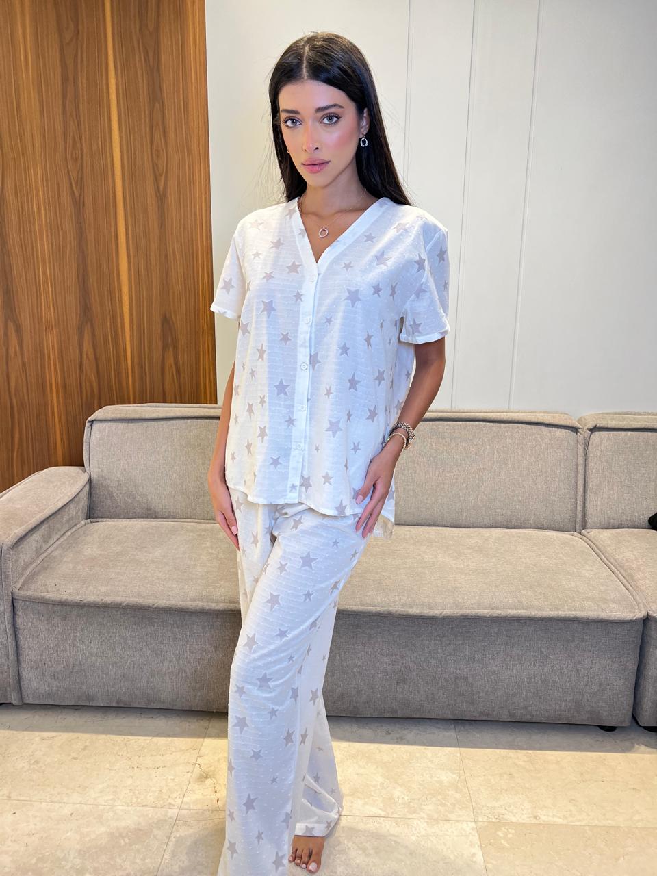 Woman in a white outfit standing in a room with a gray couch and wooden wall.