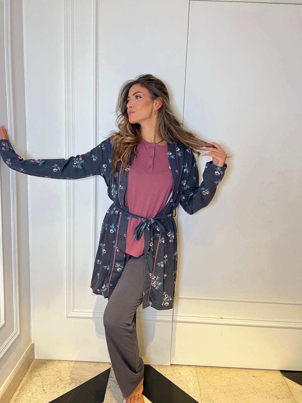 Woman wearing a floral kimono over a pink top and gray pants against a white wall.