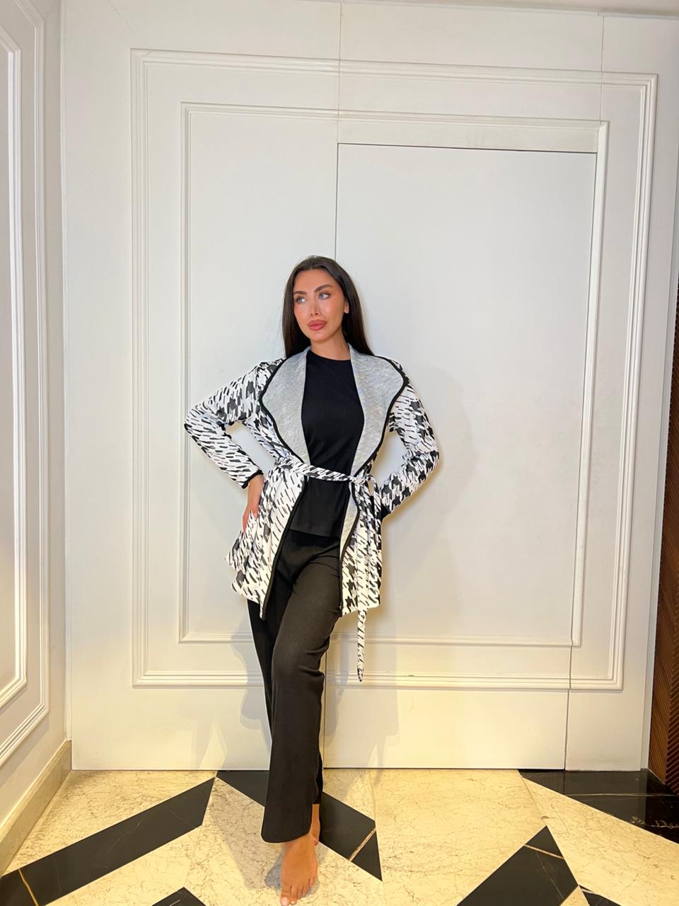 Woman wearing a black and white patterned jacket in a room with white walls and a black and white checkered floor.