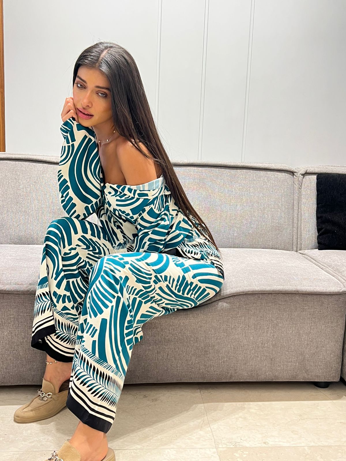 Woman sitting on a gray couch wearing a patterned outfit.