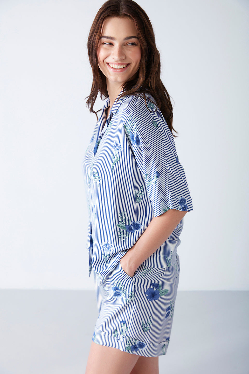 Side view of a woman smiling in a blue striped floral print pyjama set from Popjammies, highlighting the short sleeves and matching shorts.