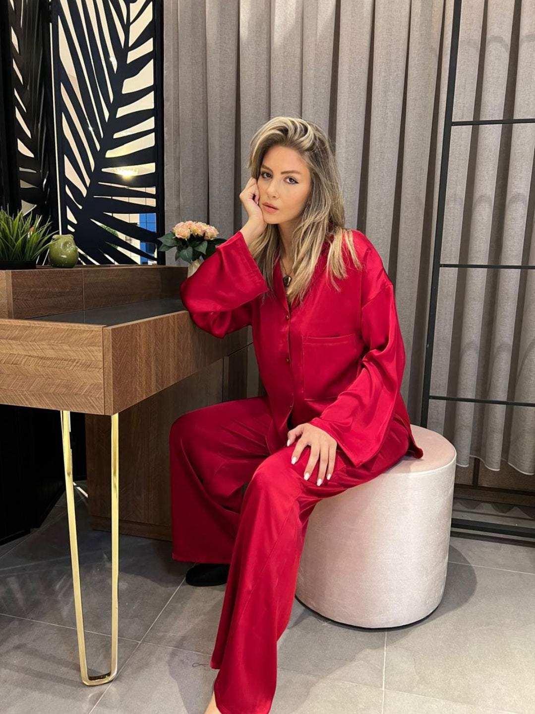 Woman wearing a red silk pyjama set by Popjammies, sitting thoughtfully at a desk.