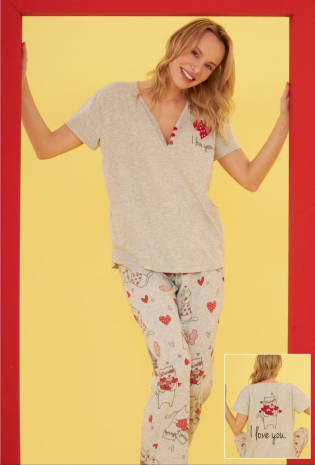 Model wearing the Popjammies "Love Cat" Pajama Set, featuring a grey top with a red polka-dot heart and "I love you" embroidery, paired with grey pants decorated with cute cat and heart prints, set against a playful, colorful background.