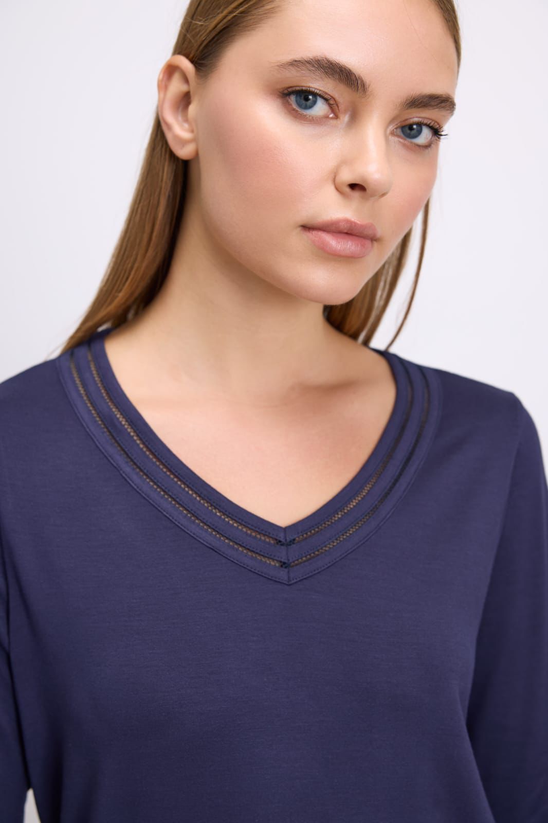 Woman wearing a dark blue long-sleeve top with a V-neckline on a light background
