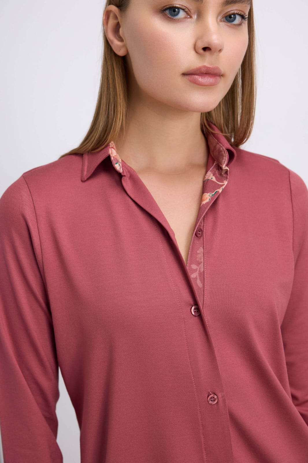 Woman wearing a pink shirt with a subtle pattern on a plain background