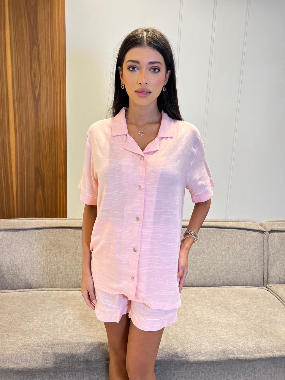 Woman wearing a pink outfit standing in a room with a couch and wooden panel.