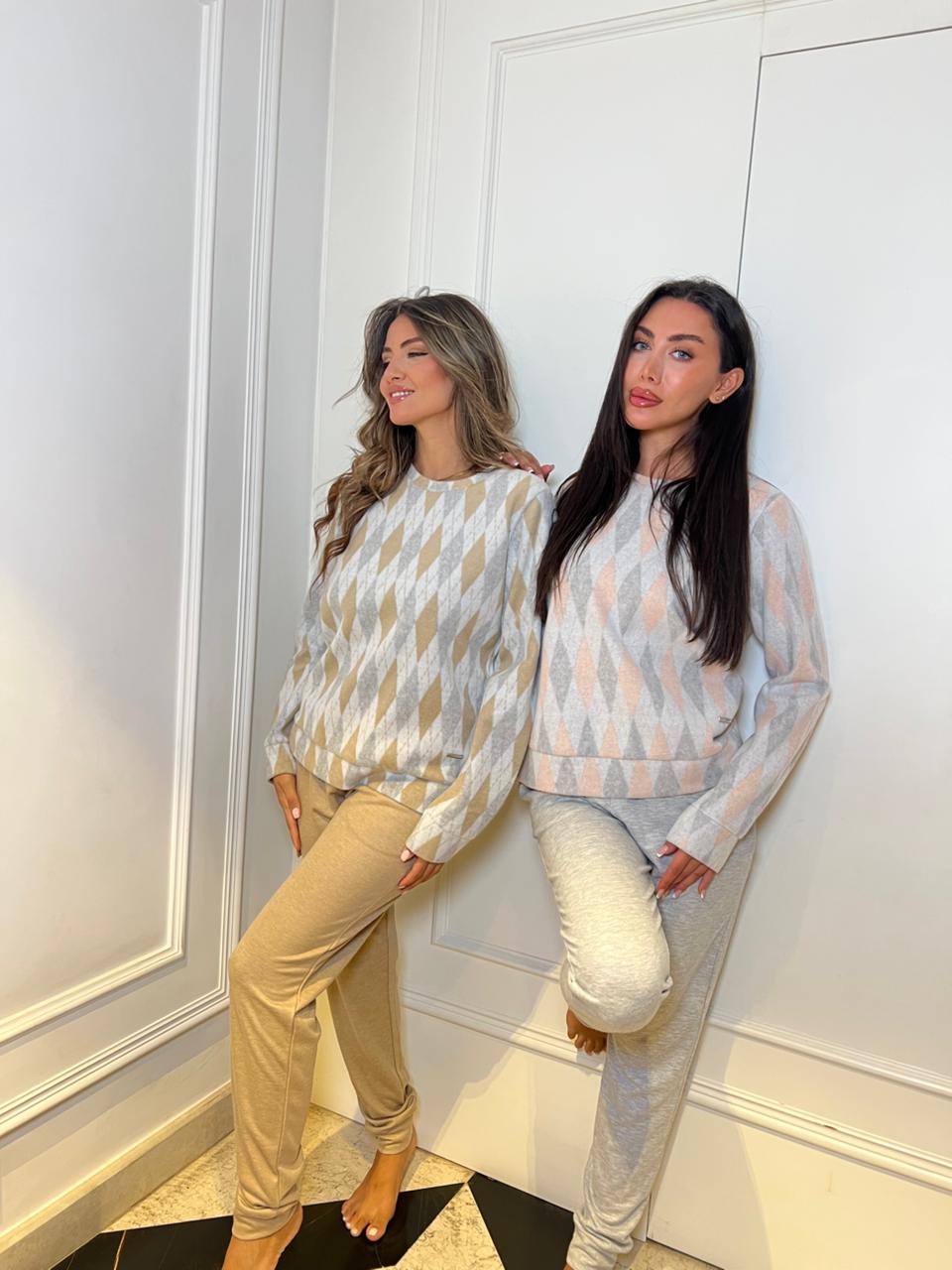 Two women wearing matching patterned tops and pants standing against a white wall.