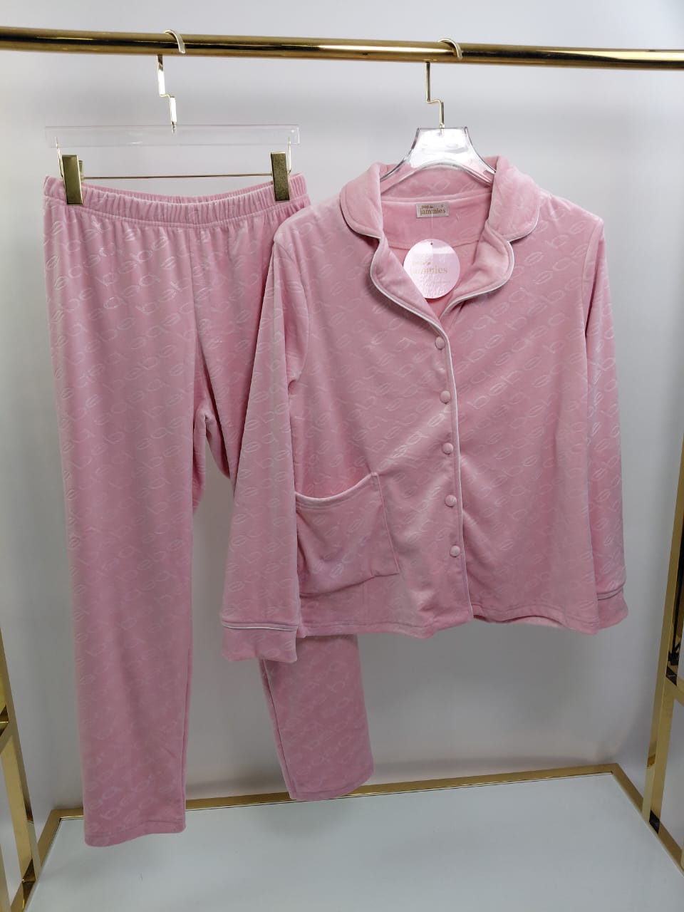 Pink pajama set with top and pants hanging on a rack against a white background