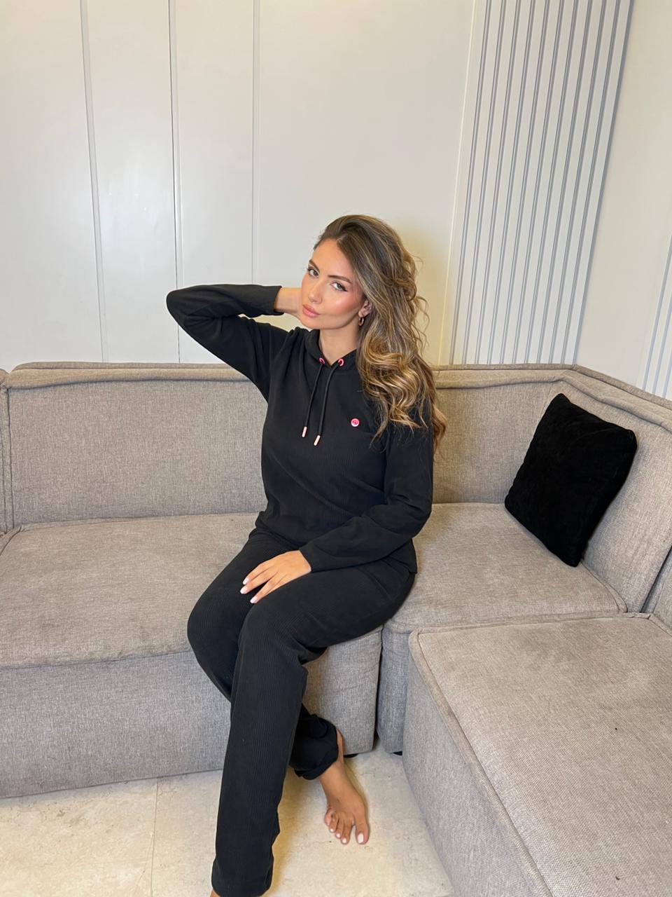 Woman in black outfit sitting on a gray sofa with a neutral background