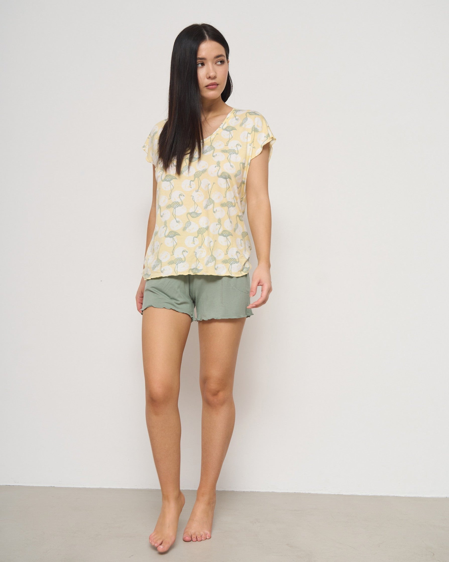 Woman standing in a Popjammies yellow flamingo print top and green shorts, showcasing a comfortable and stylish pyjama set.