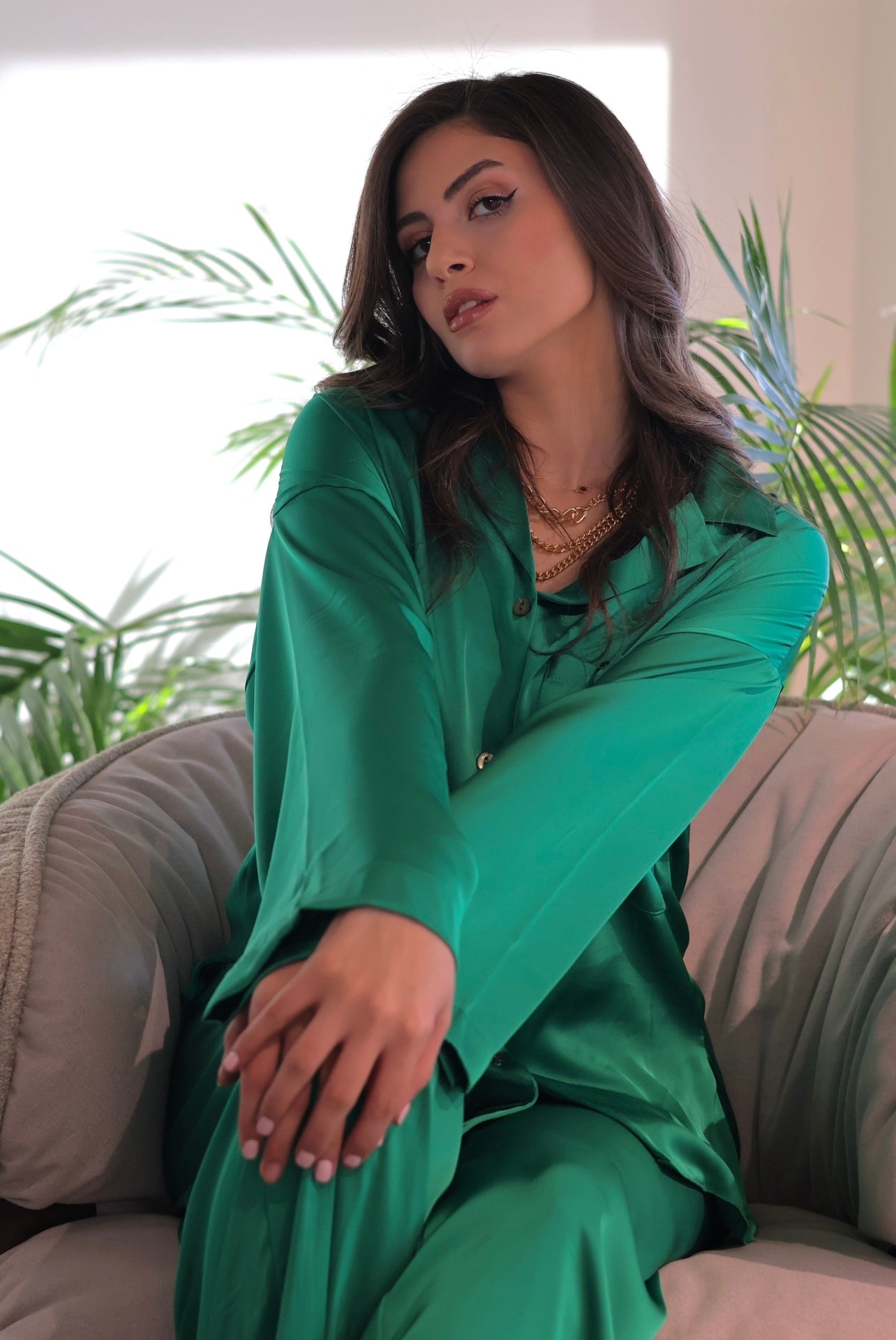 Woman in a green silk pyjama set by Popjammies, sitting with her arm up, posing stylishly.