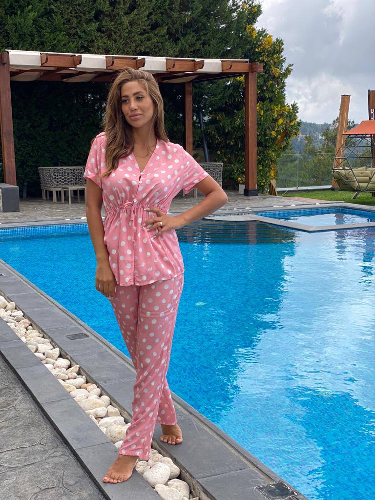 Woman wearing the Popjammies Pink Polka Dot Pajama Set, standing by a poolside, featuring a pink button-down top with white polka dots and matching pants.