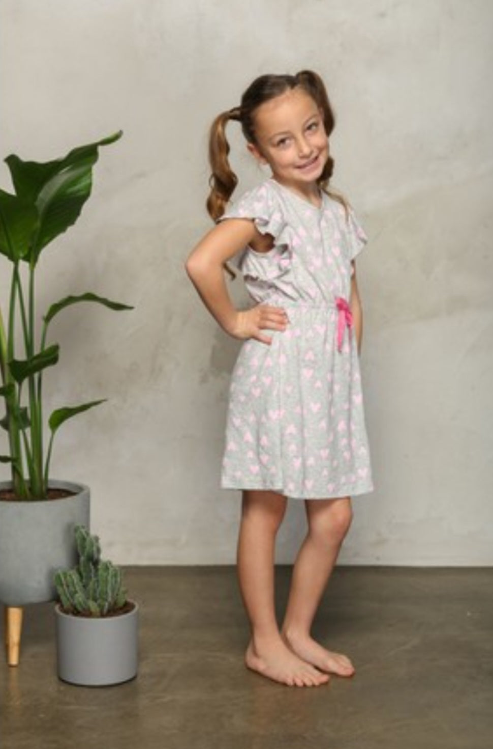 Child wearing a Popjammies dress with heart dots and a pink ribbon, smiling.