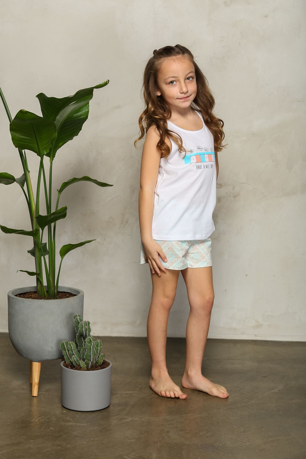 Girl wearing white tank top pajamas with shorts, standing and posing with her hands on her hips.