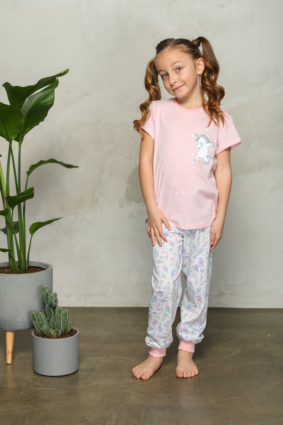Girl wearing pink unicorn-themed pyjama set standing next to a plant
