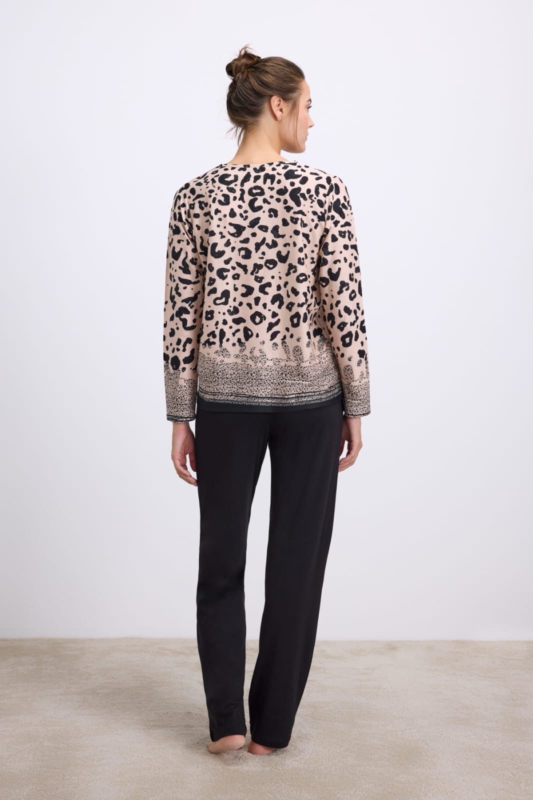 Woman wearing a leopard print top and black pants on a plain background