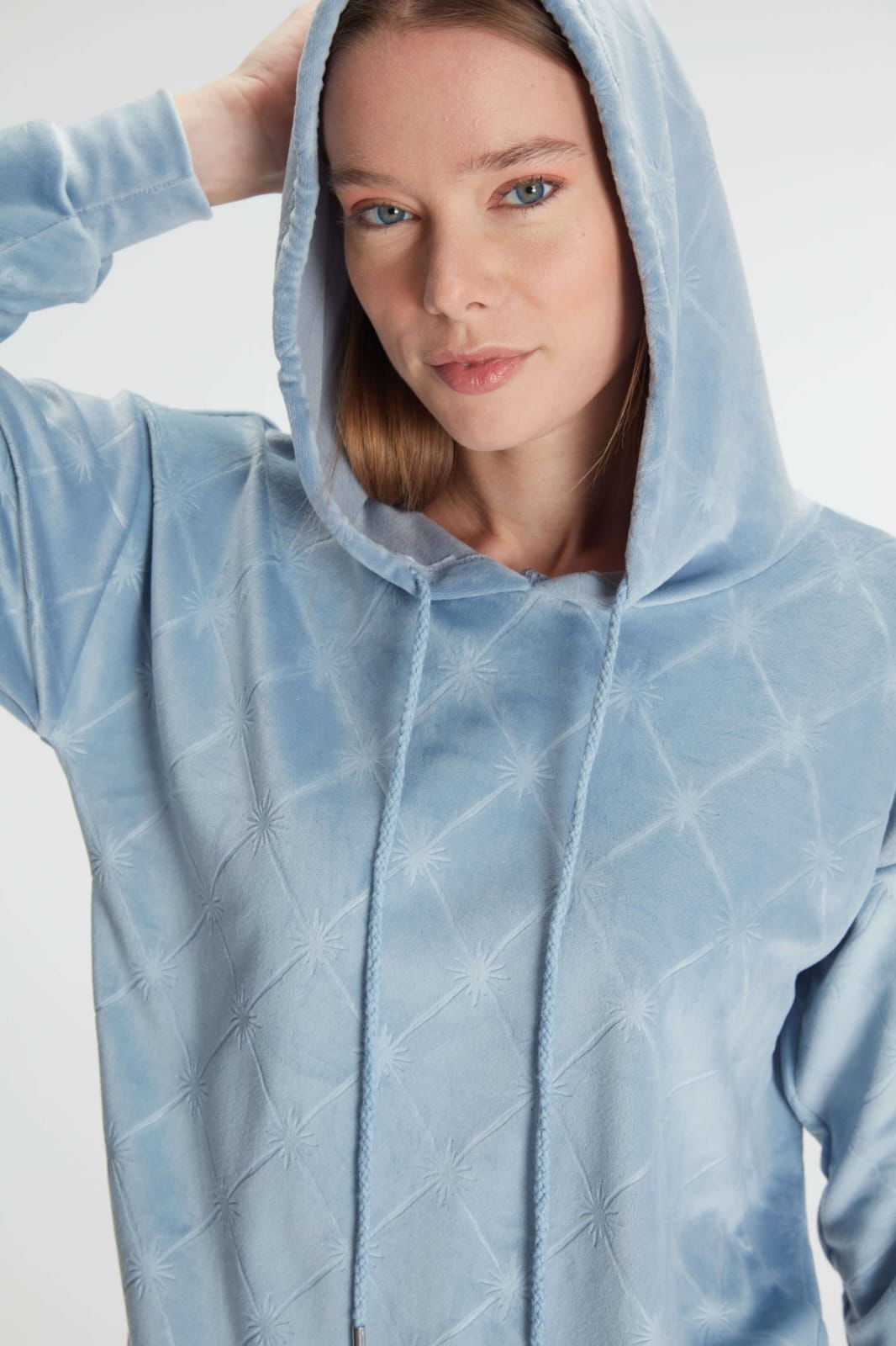 Person wearing a light blue quilted hoodie against a white background