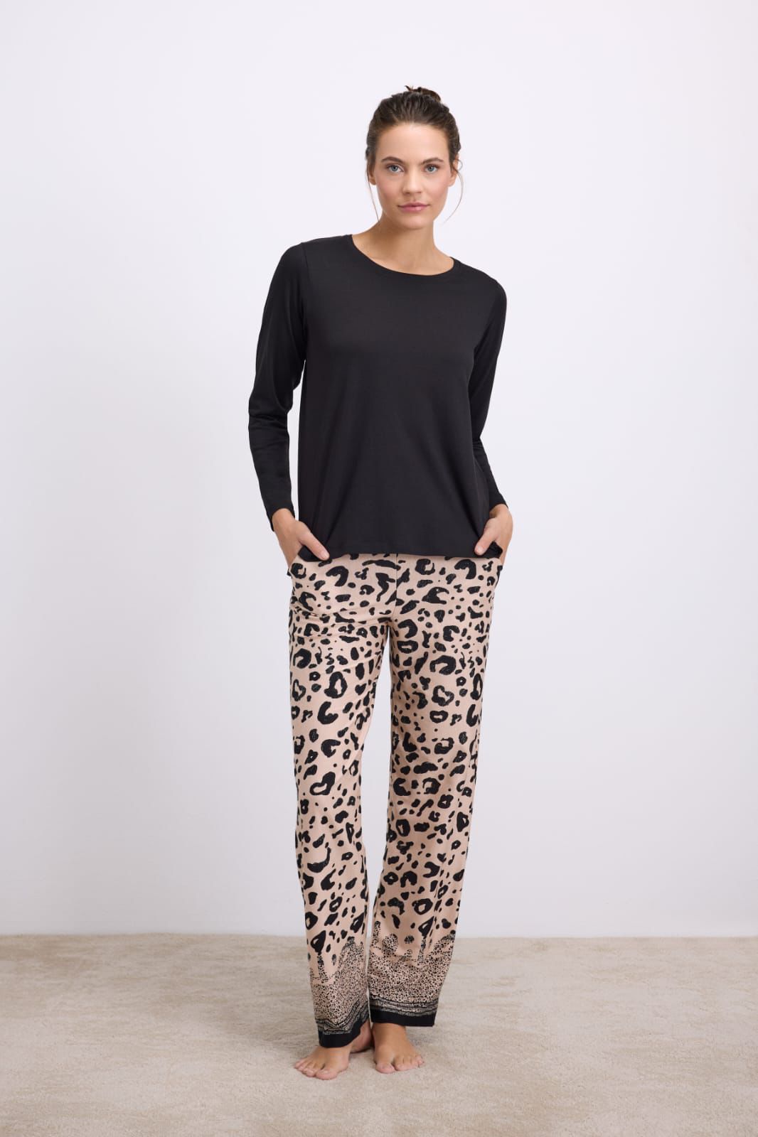 Woman wearing a black long-sleeve top and leopard print pants on a white background