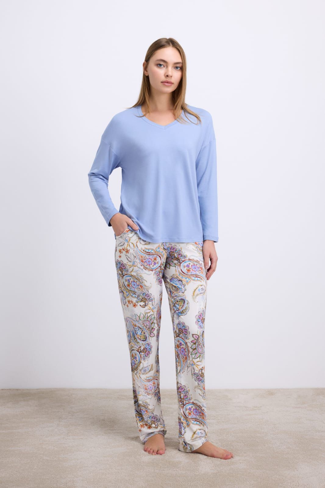 Woman wearing a light blue top and patterned pants on a plain background