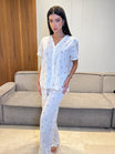 Woman in a white outfit standing in a room with a gray couch and wooden wall.