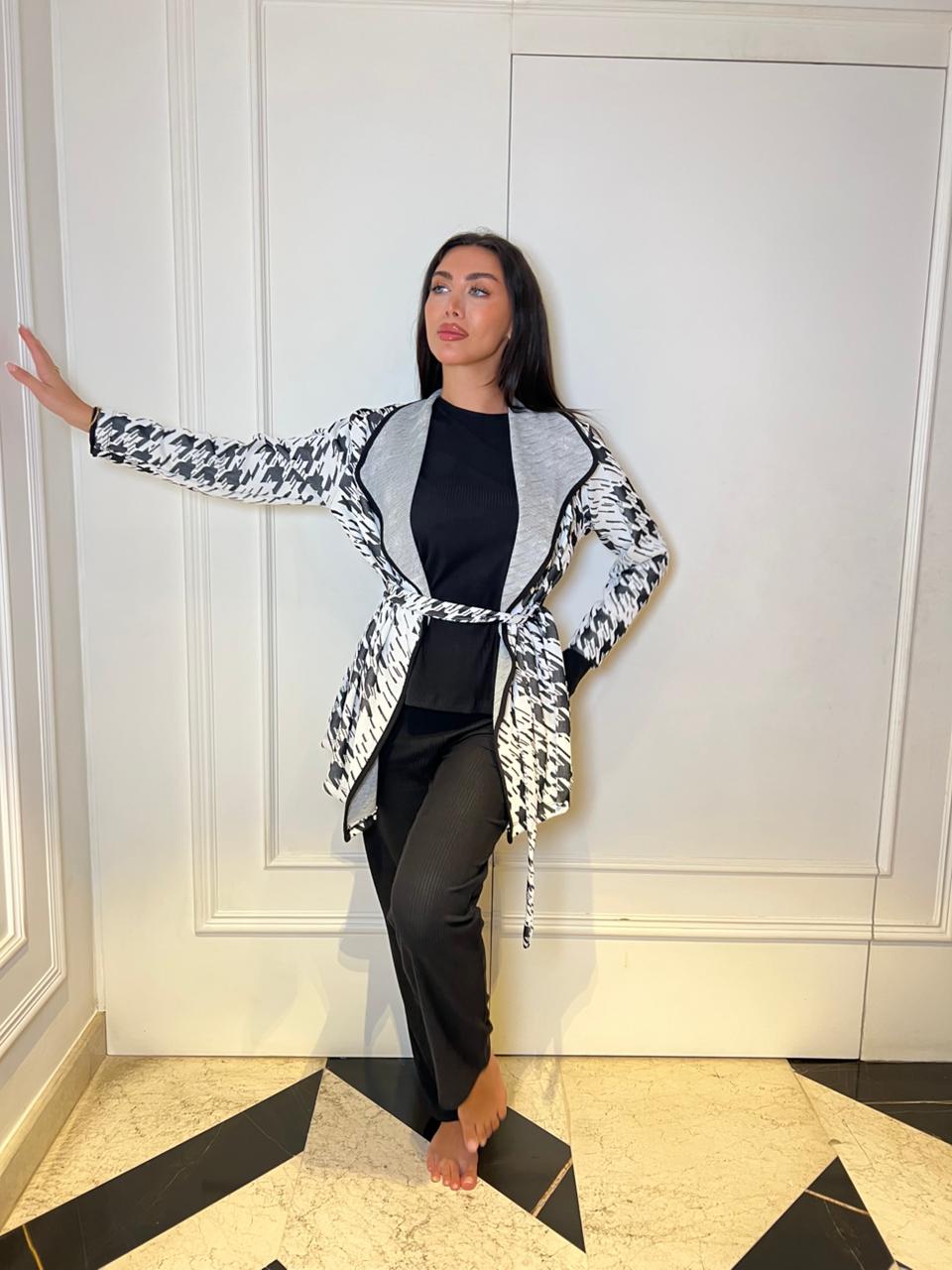 Woman posing in a stylish outfit with a patterned cardigan against a white wall.
