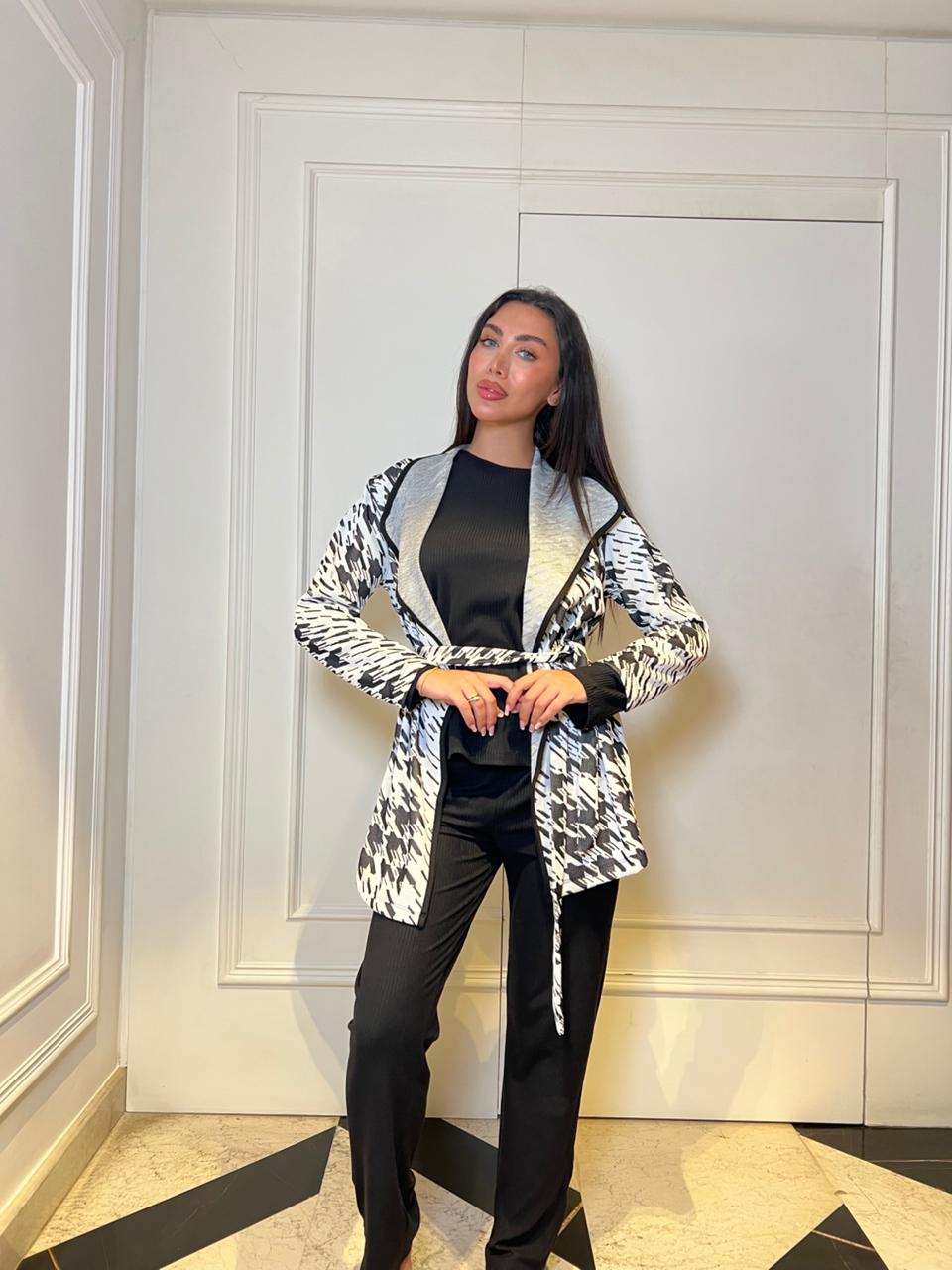 Woman wearing a patterned cardigan over a black top and pants in an indoor setting.