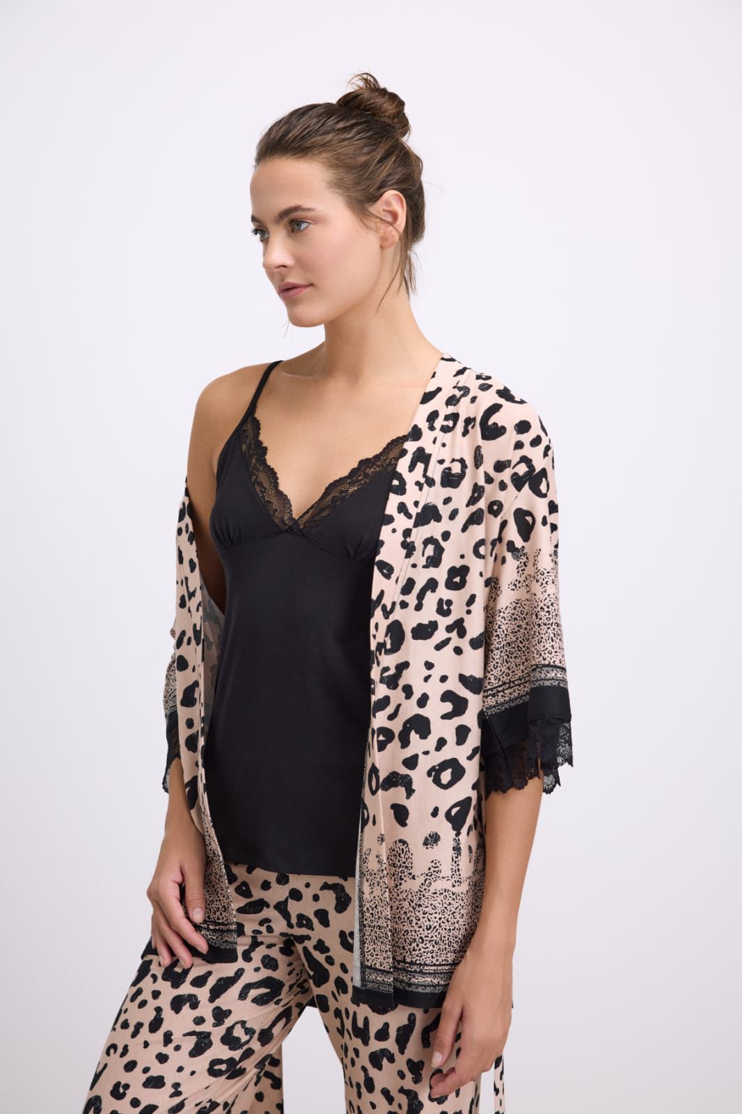 Woman wearing a leopard print kimono over a black top and pants on a white background