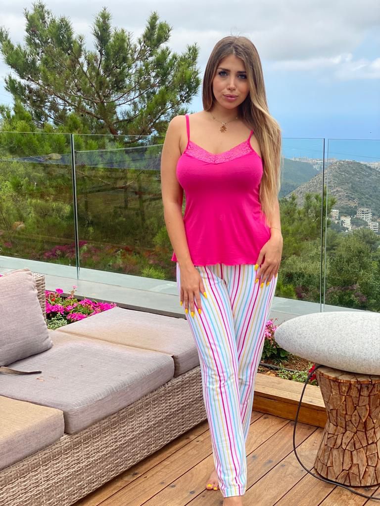 Woman in a pink camisole with lace trim and white striped pants, standing on a patio.