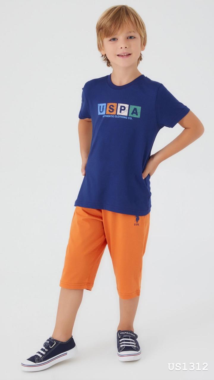 Boy wearing Popjammies pyjama set with a navy blue tee featuring a colorful "USPA Authentic Clothing Co." logo and orange shorts, standing with hands on hips.