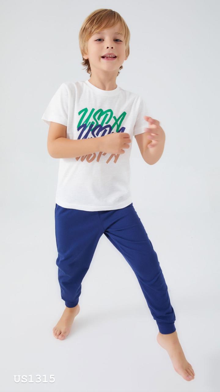 Boy wearing Popjammies white t-shirt with colorful "USPA" graphics and navy jogger pants, standing and smiling.