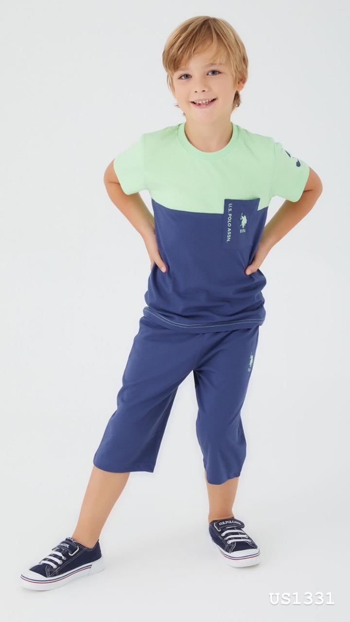  Boy wearing a mint green and navy color block top with a front pocket and navy pants, standing and smiling.