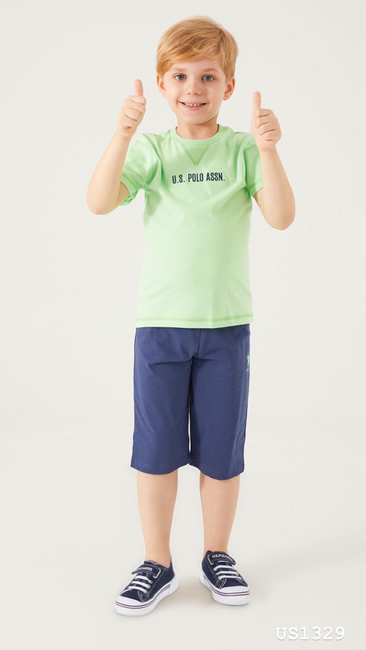Boy wearing a green top with "U.S. POLO ASSN." printed on the front and navy pants, smiling and giving thumbs up.