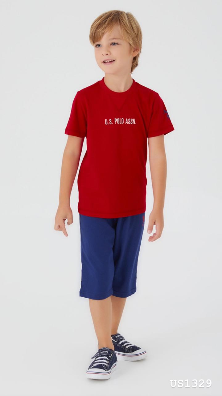 Boy wearing a red top with "U.S. POLO ASSN." printed on the front and navy pants, smiling and standing.