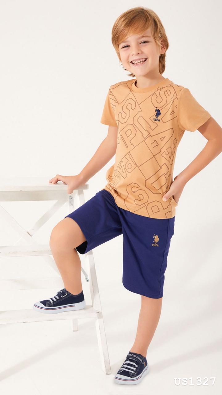 Child wearing Popjammies USPA Graphic Pyjama Set with mustard top and navy shorts sitting on a white ladder and smiling