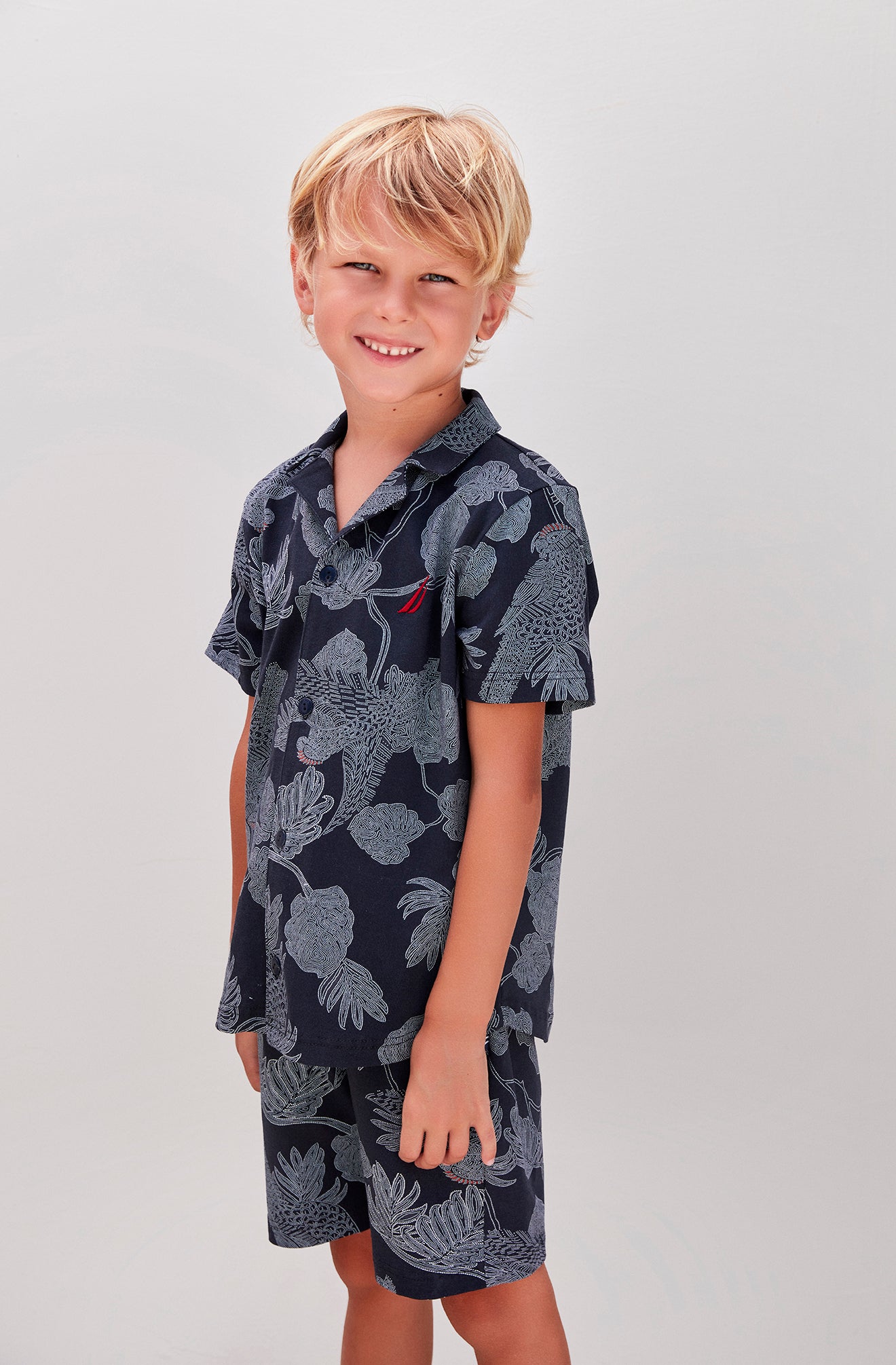 Blonde boy wearing a navy blue nautical pajama set with ocean-inspired patterns, smiling.