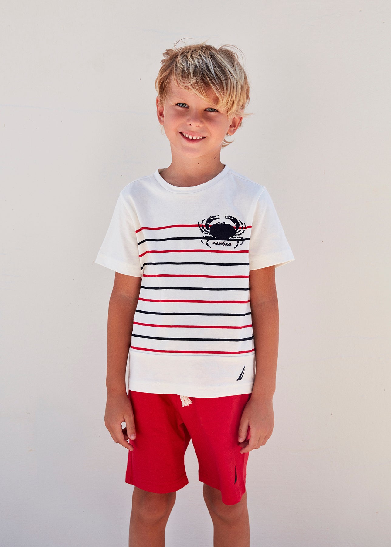 Boy wearing white short-sleeve top with red and navy patterns and red shorts