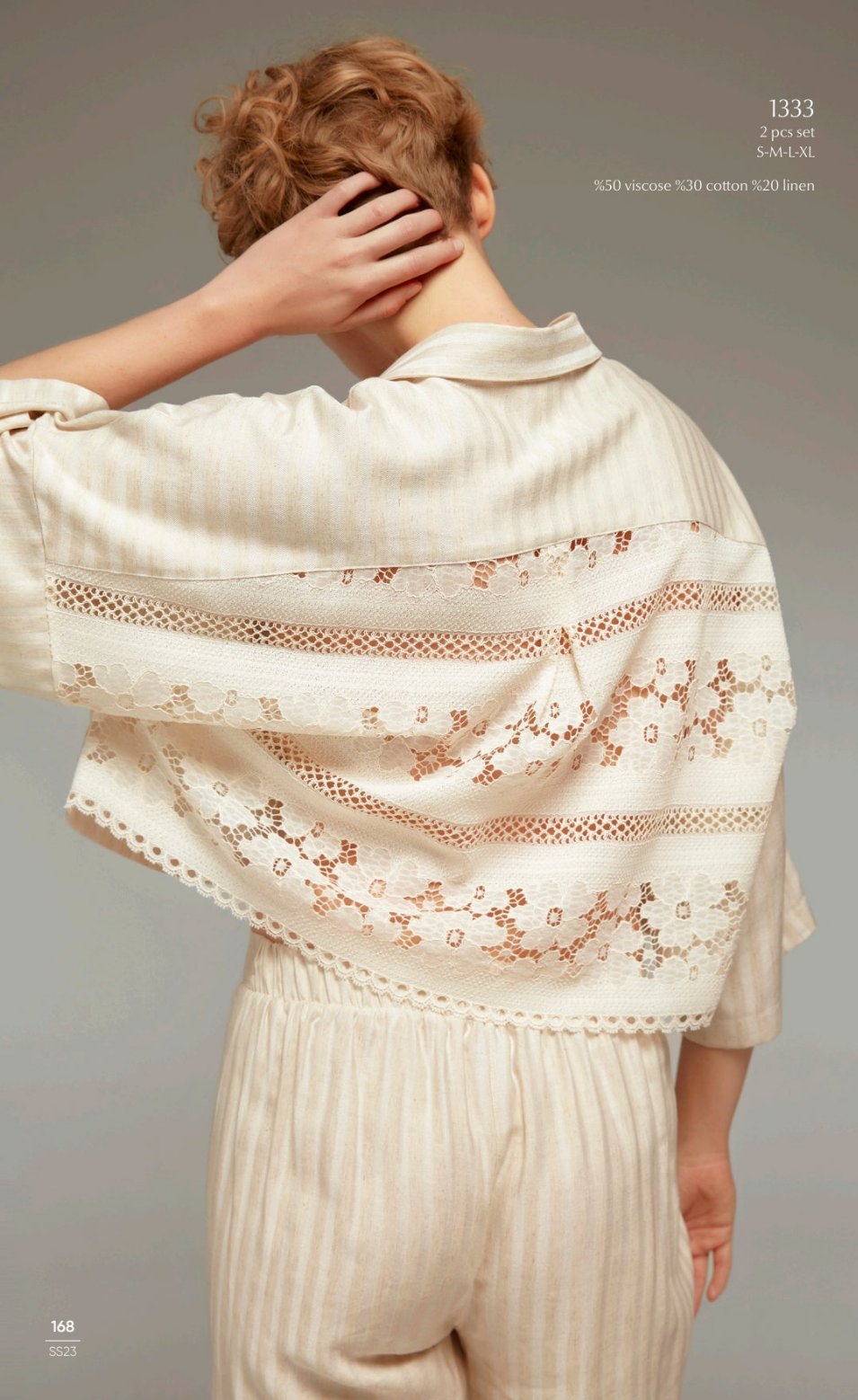 Model showing the back view of the Popjammies 1333 Two-Piece Pyjama Set in cream, featuring intricate lace detailing on the back of the button-down cropped top and matching high-waisted trousers.