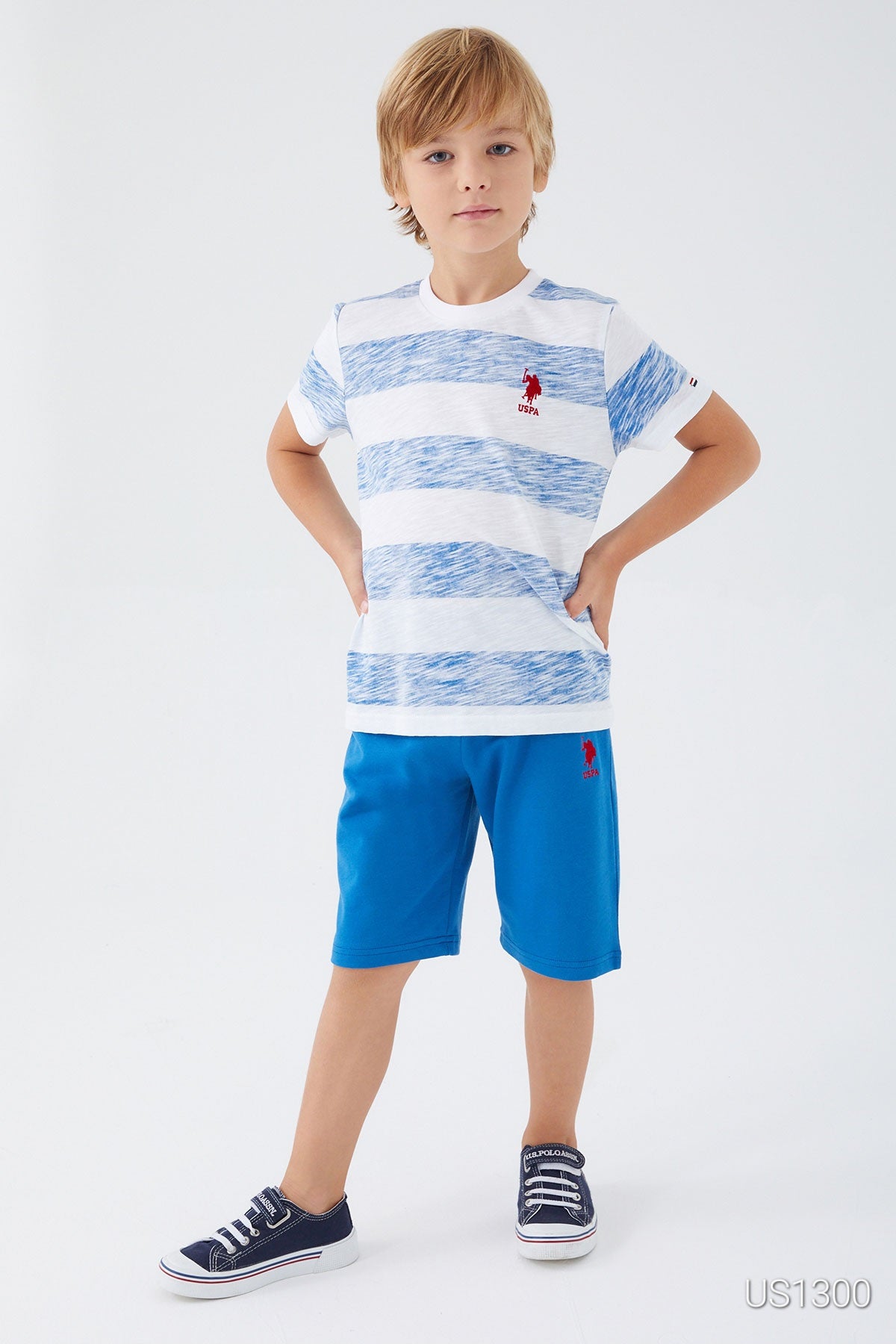 Child wearing Popjammies pyjama set with white top and large light blue patterns, paired with blue shorts with his hands on his hips. 