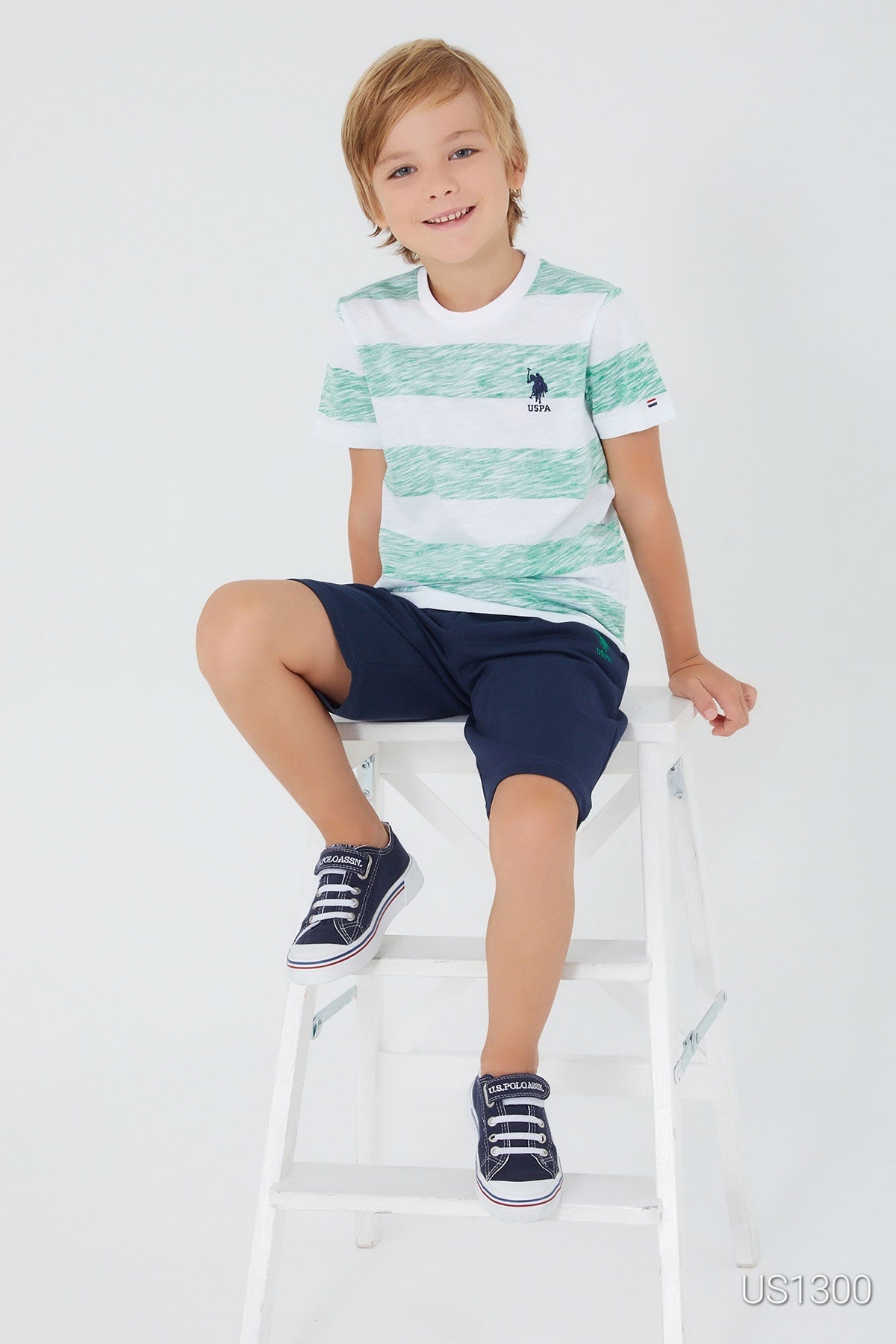 Child sitting on a white chair wearing Popjammies pyjama set with white top and large green patterns, paired with navy shorts