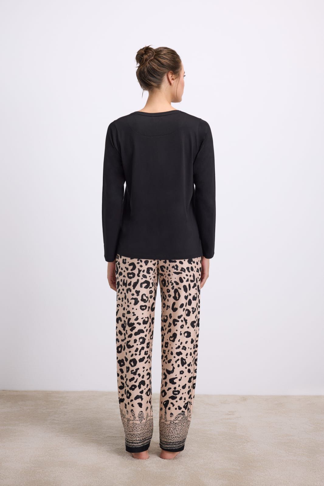 Person wearing a black top and leopard print pants on a plain background