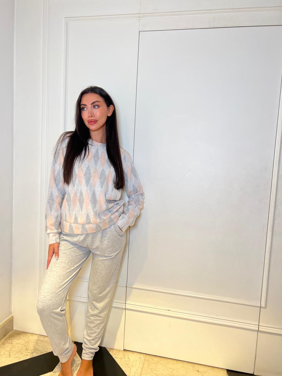 Woman in a light gray outfit standing against a white wall.