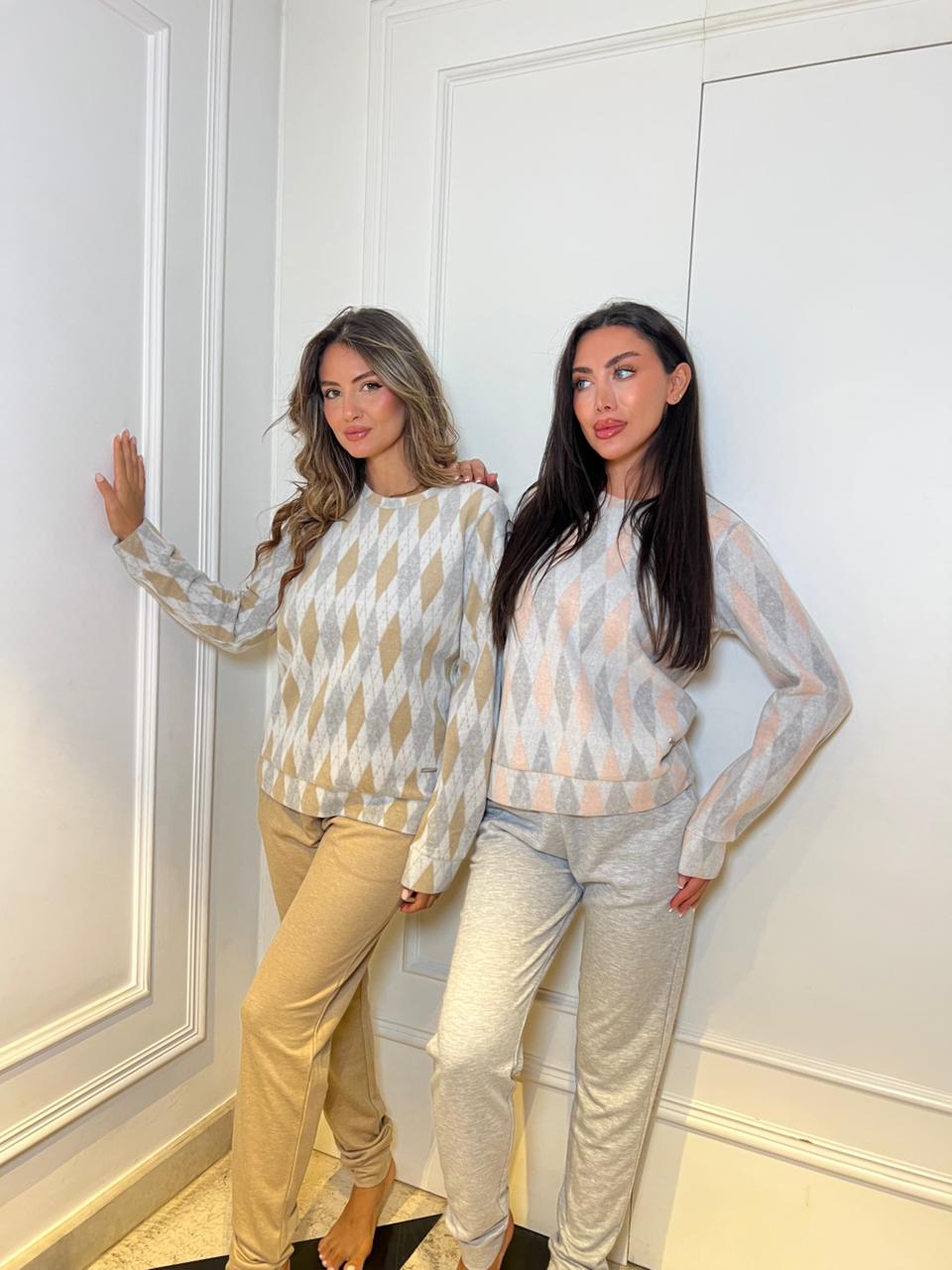 Two women wearing matching patterned tops and pants standing against a white paneled wall.