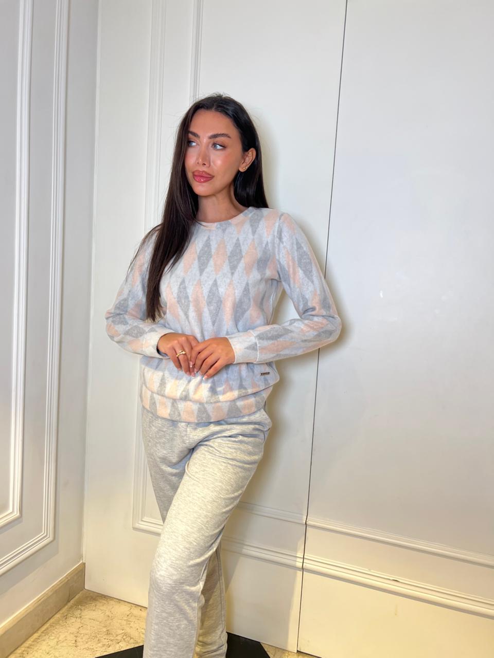 Woman wearing a light-colored patterned sweater and pants against a white wall.