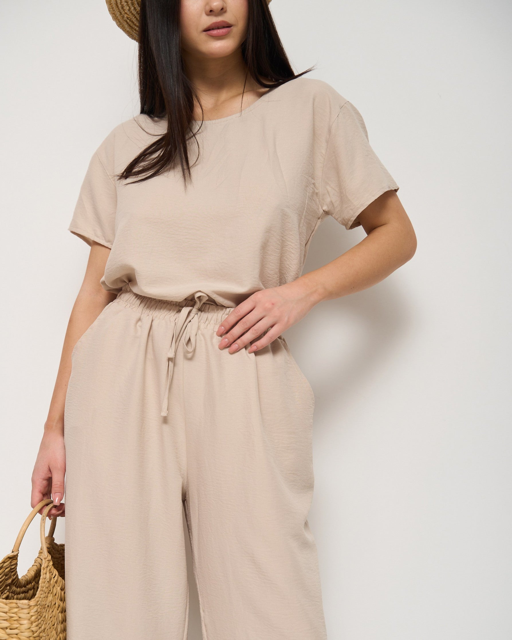 Close-up view of a model wearing a beige pyjama set with a drawstring waist and holding a straw bag, highlighting the soft fabric and relaxed fit by Popjammies.