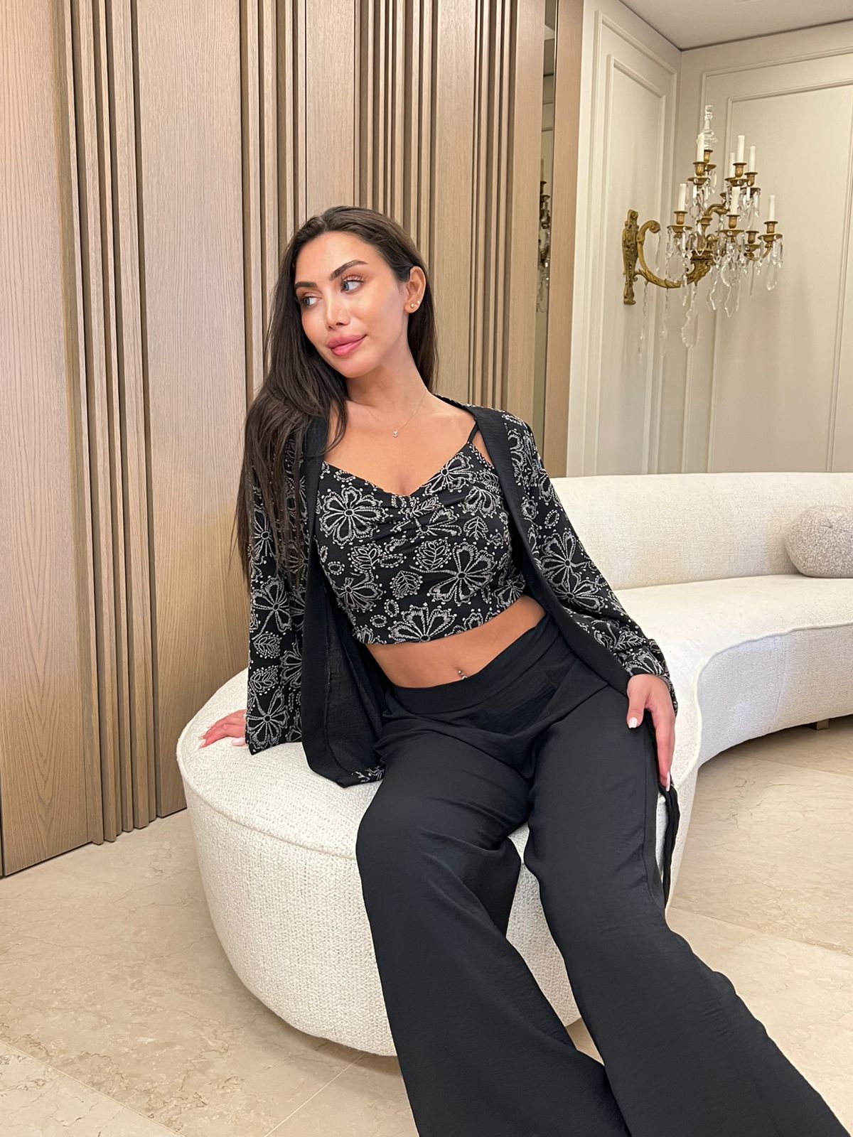 3-piece women’s pyjama set featuring a soft top - Woman sitting on a white chair in an elegant room with a chandelier.