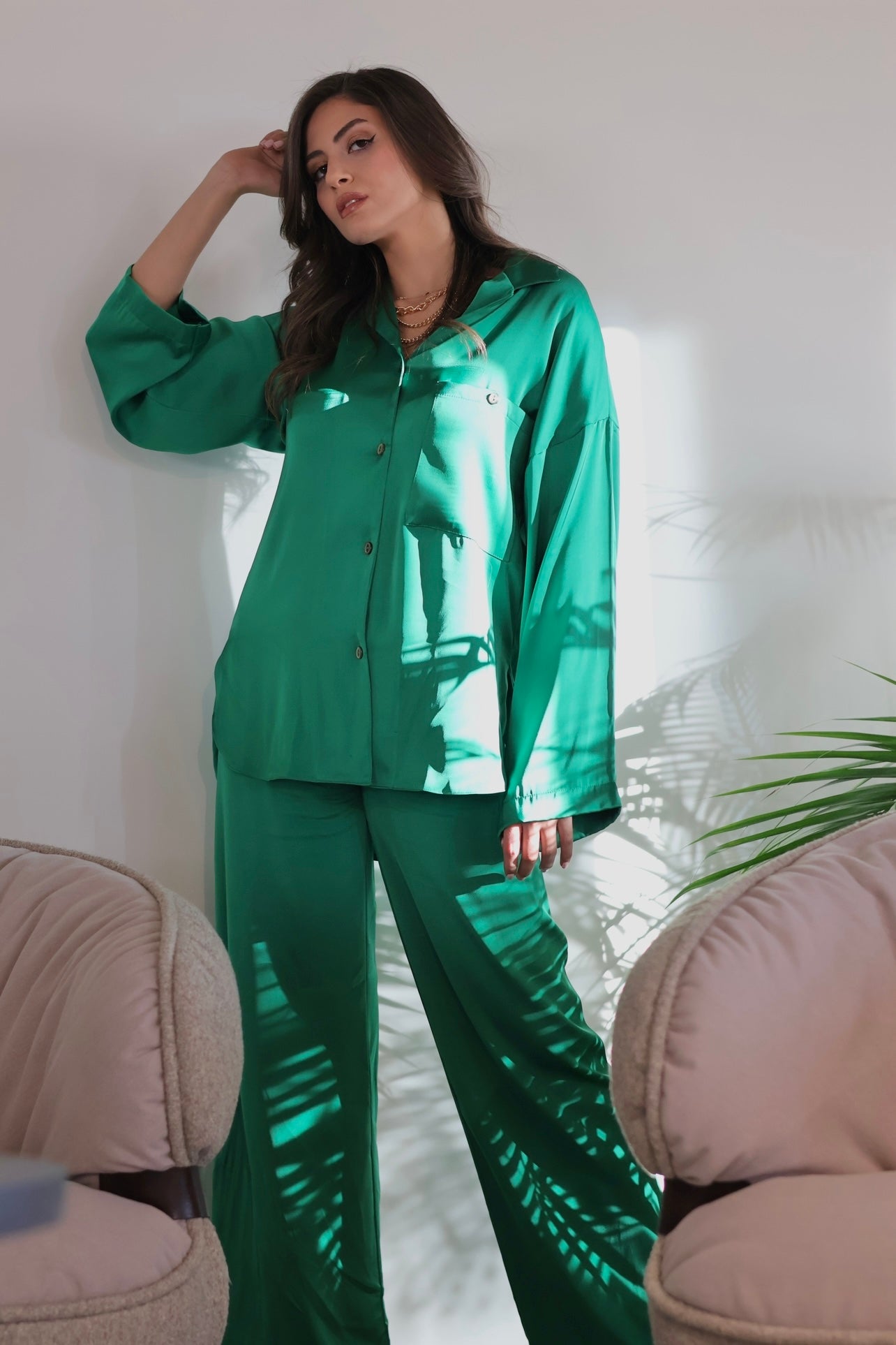 Woman wearing a green silk pyjama set by Popjammies, standing and posing with her hand on her head.