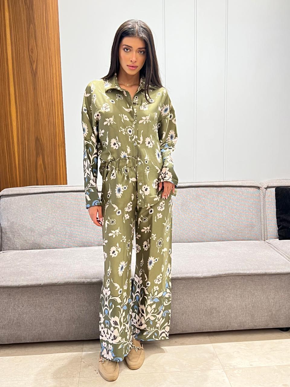 Woman wearing a green floral jumpsuit standing in a room with a gray couch.