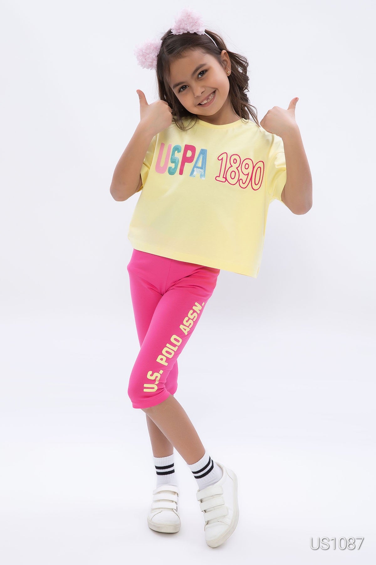 Girl wearing a yellow top with pink pantacourt in front of a plain background