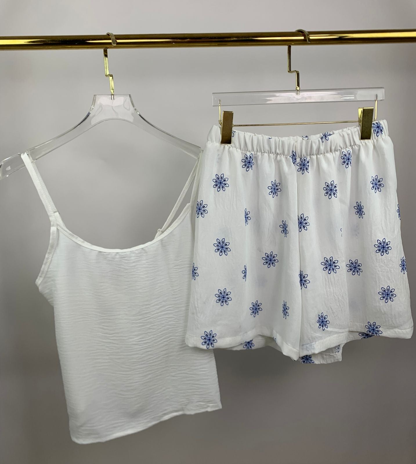 White tank top and floral shorts on hangers against a gray background